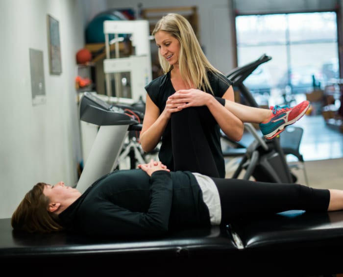 A woman performs an exercise under the guidance of a physical therapist in a clinical setting.