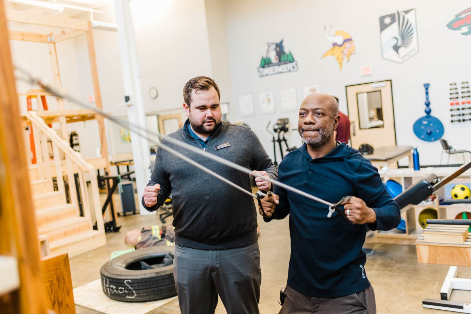 occupational therapist assists patient performing upper back exercise in gym