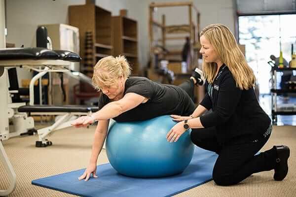 Occupational therapist assisting patient with ball exercise for trunk stability