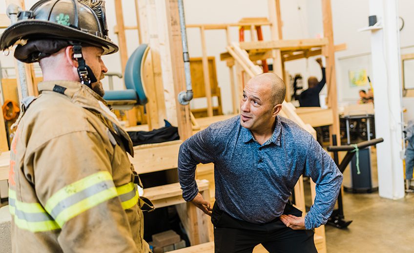 physical therapist explaining body mechanics techniques to firefighter