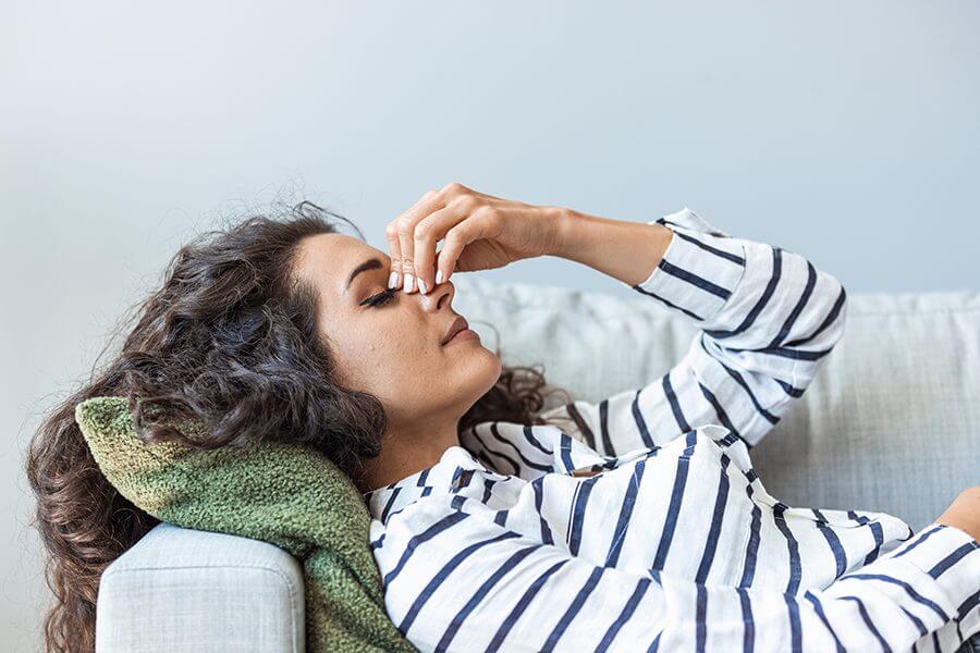 Woman lying on couch pinching her nose area due to headache
