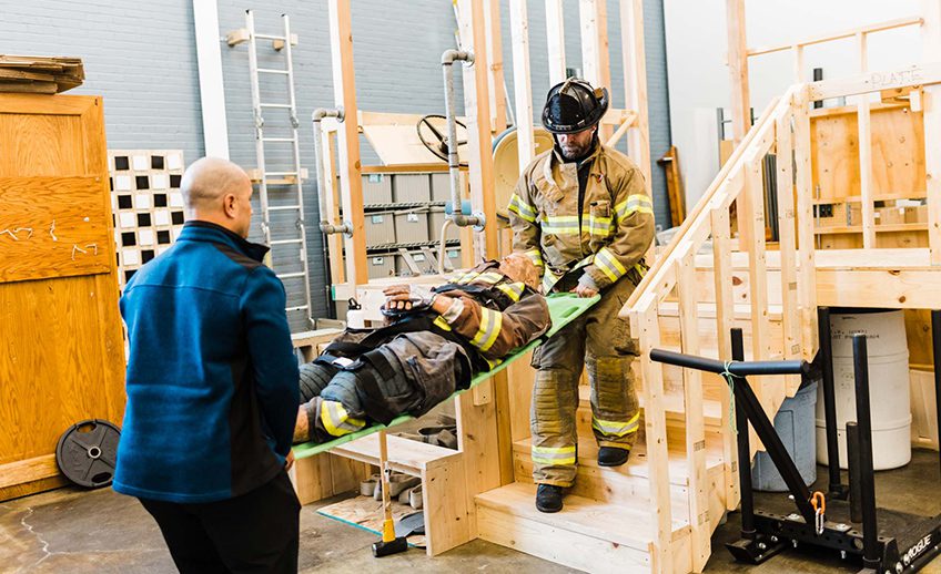 physical therapist and firefighter practicing patient transport in gym